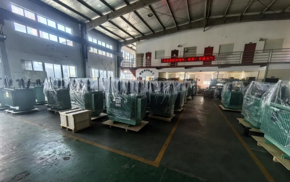 Dozens of green transformers wrapped in plastic on wooden skids ready for dispatch inside the Baitong Electric 1000 kva oil immersed transformer factory.
