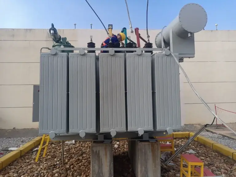 A field technician commissioning a heavy-duty oil immersed transformer in China by Baitong Electric, showing concrete plinths, corrugated radiators, and a gravel containment pit.