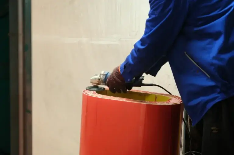 A skilled worker in a blue uniform polishing the edge of a newly cast red dry type transformer coil to ensure a perfectly smooth finish.