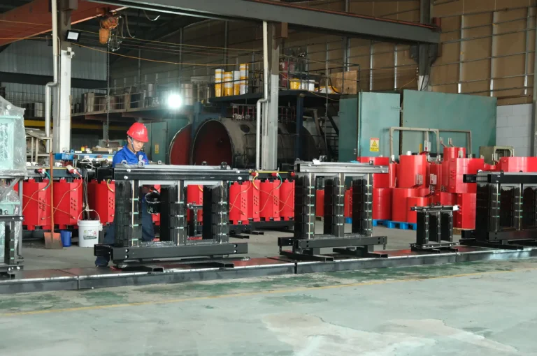 A Baitong Electric worker wearing a red hard hat assembling magnetic cores on the floor of a real dry type transformer factory.