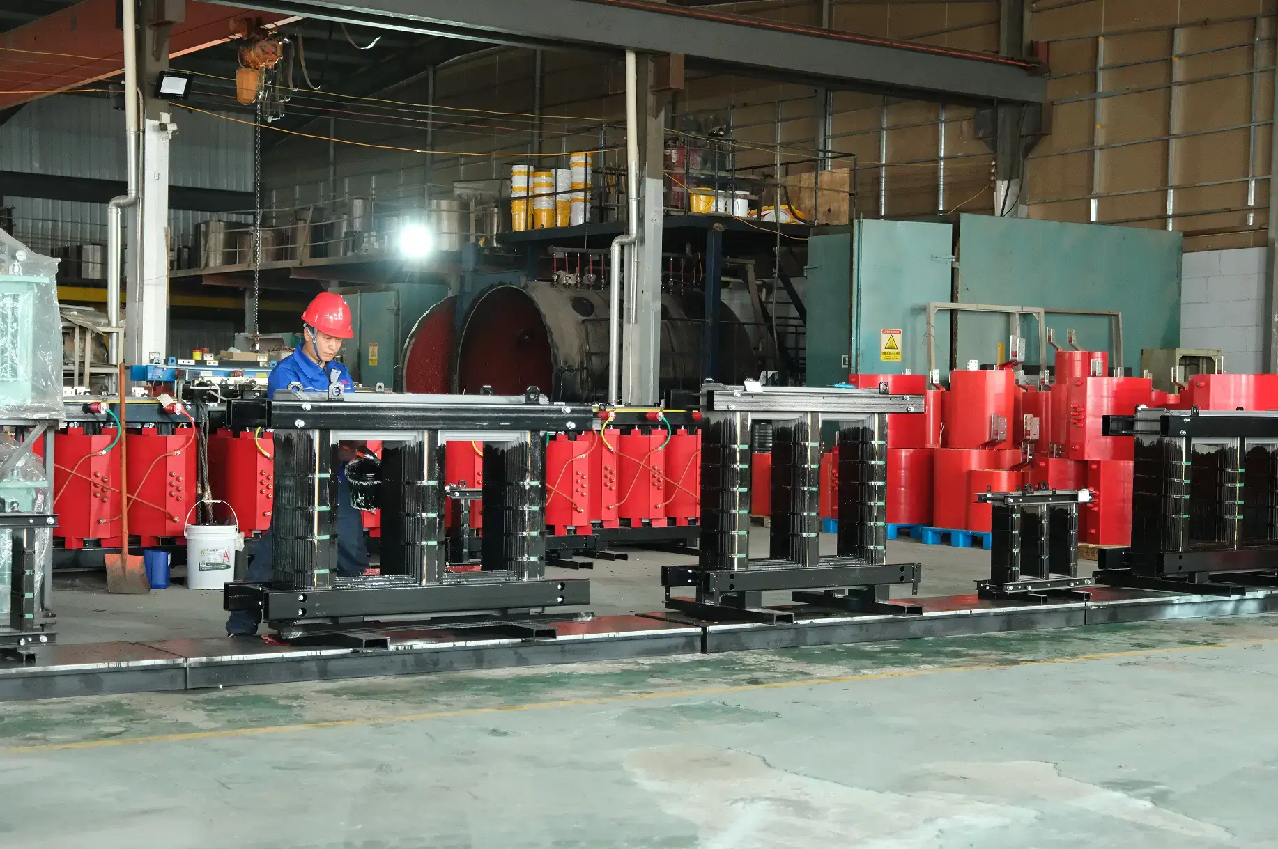 A Baitong Electric worker wearing a red hard hat assembling magnetic cores on the floor of a real dry type transformer factory.