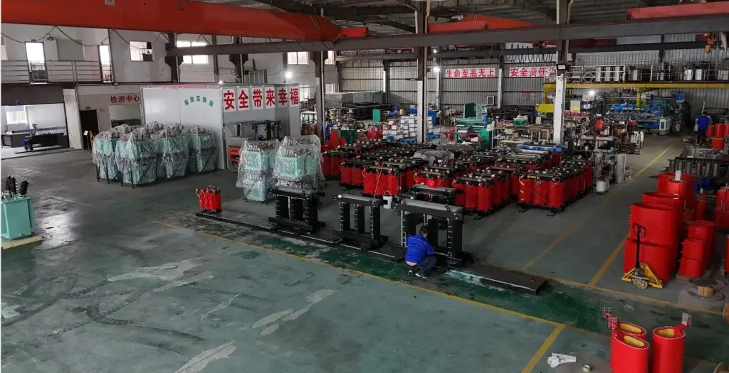 A wide shot of the Baitong Electric factory floor showing a technician assembling a black magnetic core next to rows of red cast resin coils, showcasing our capabilities as a dry-type transformer manufacturer.