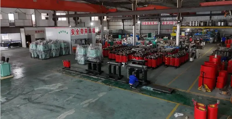 A wide shot of the Baitong Electric factory floor showing a technician assembling a black magnetic core next to rows of red cast resin coils, showcasing our capabilities as a dry-type transformer manufacturer.