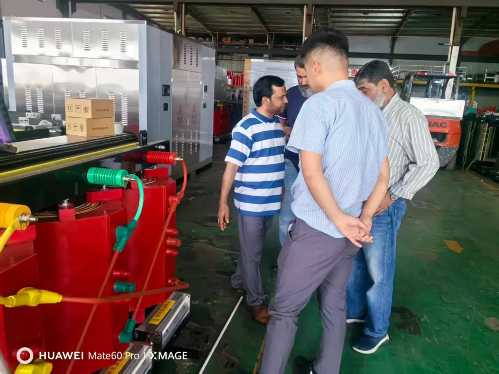 International clients visiting the Baitong Electric factory floor to inspect a red wholesale three phase dry type transformer during a guided tour.