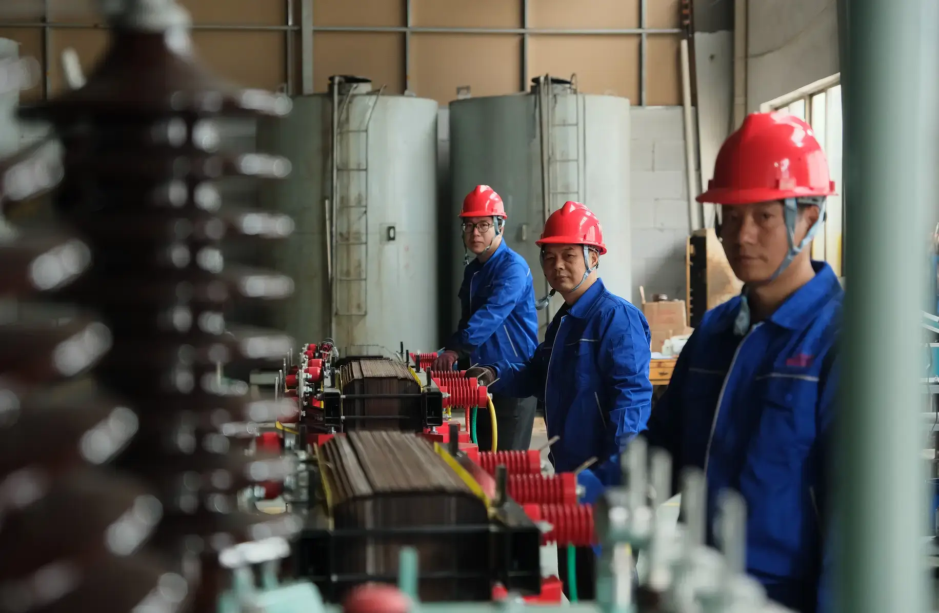 A dedicated transformer manufacturing team wearing blue uniforms and red hard hats assembling a core structure on the Baitong Electric factory floor.
