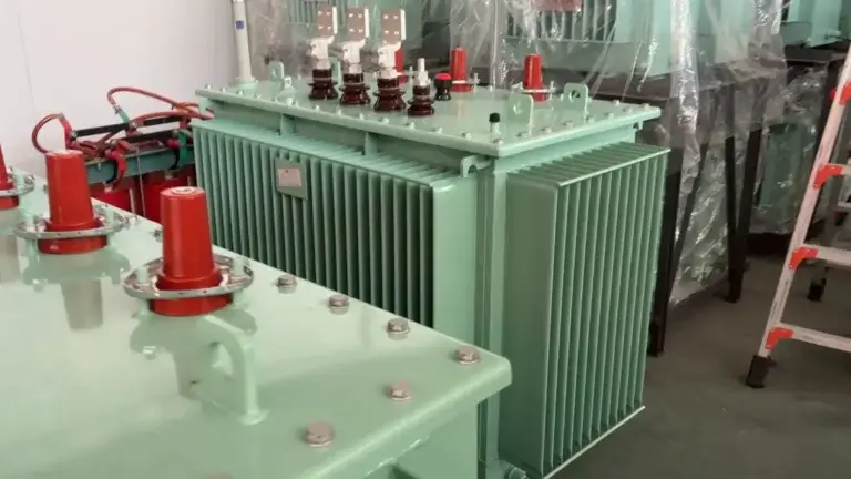 Close up view of a precise oil immersed transformer assembly showing flat connection terminals, lifting lugs, and red protective caps at the Baitong Electric factory.