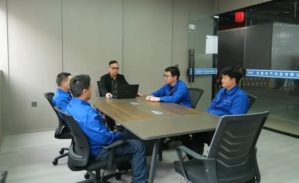 The expert transformer engineering team at Baitong Electric discussing custom power grid solutions in a glass meeting room overlooking the factory floor.
