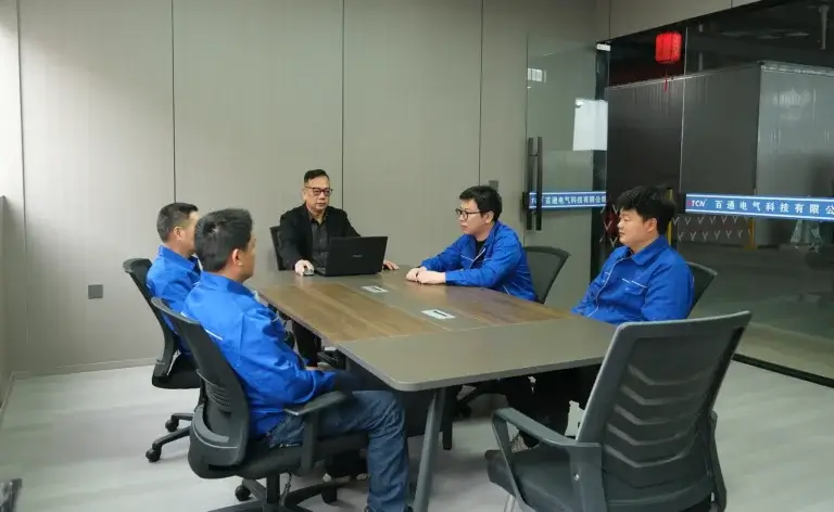 The expert transformer engineering team at Baitong Electric discussing custom power grid solutions in a glass meeting room overlooking the factory floor.