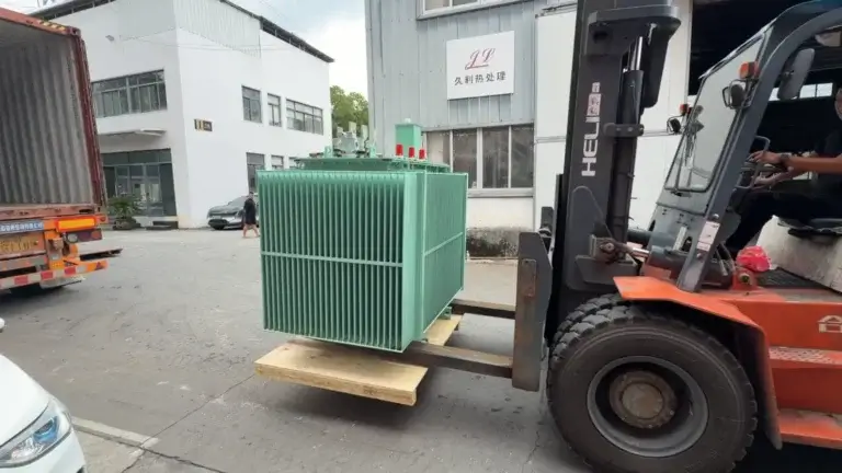 A heavy orange forklift loading a green 110kv oil immersed power transformer into a shipping container at the Baitong Electric factory courtyard.