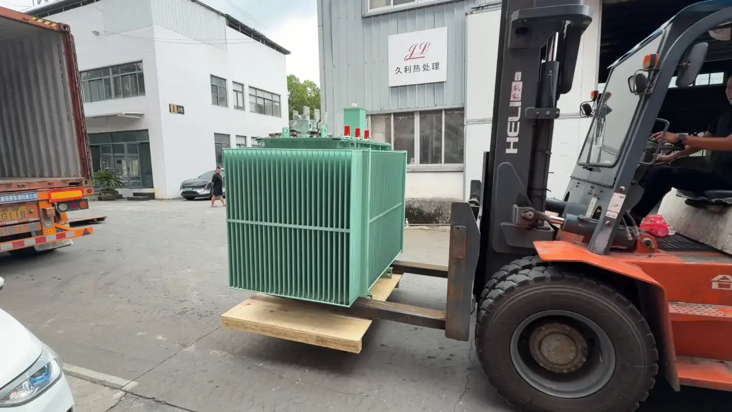 A heavy orange forklift loading a green 110kv oil immersed power transformer into a shipping container at the Baitong Electric factory courtyard.