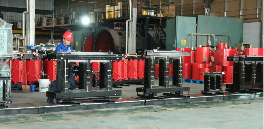 A factory worker in a blue uniform and red hard hat painting steel core frames inside the Baitong Electric 100 kva dry type transformer factory.