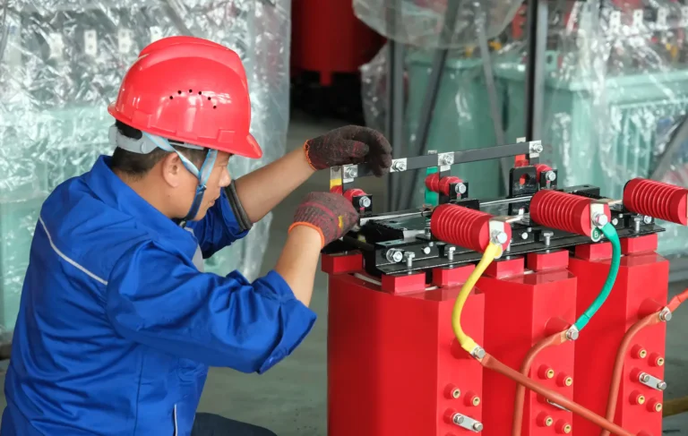 A Baitong Electric technician wearing a blue uniform and red hard hat carefully assembling the red cast resin coils of a dry type transformer.