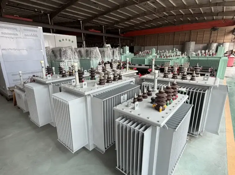 A row of newly assembled grey oil-filled transformers with brown ceramic bushings and cooling fins on the Baitong Electric factory floor.