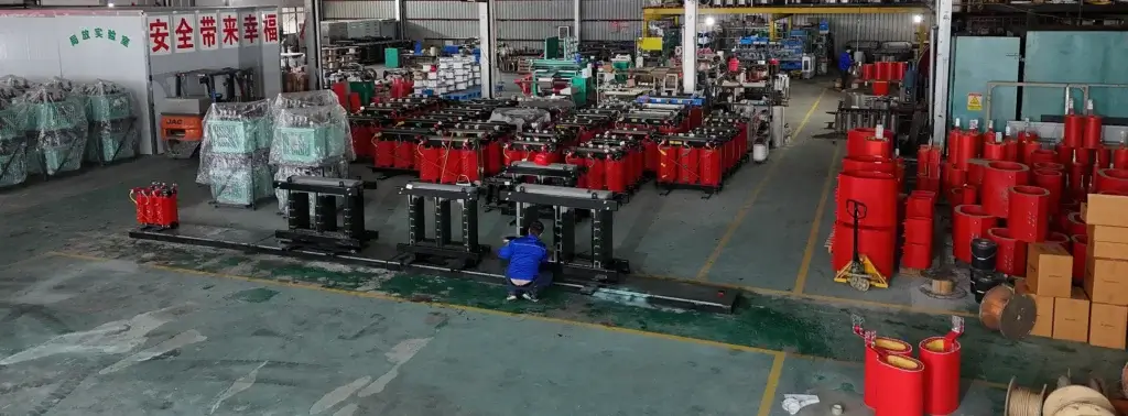 A wide view of the Baitong Electric factory floor showing a worker assembling steel cores alongside dozens of red cast resin wholesale 3 phase dry type transformers.