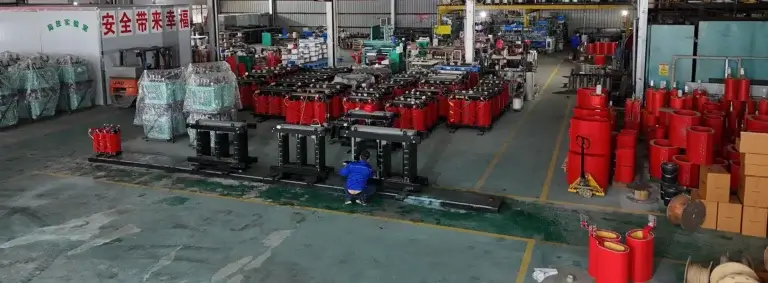 A wide view of the Baitong Electric factory floor showing a worker assembling steel cores alongside dozens of red cast resin wholesale 3 phase dry type transformers.