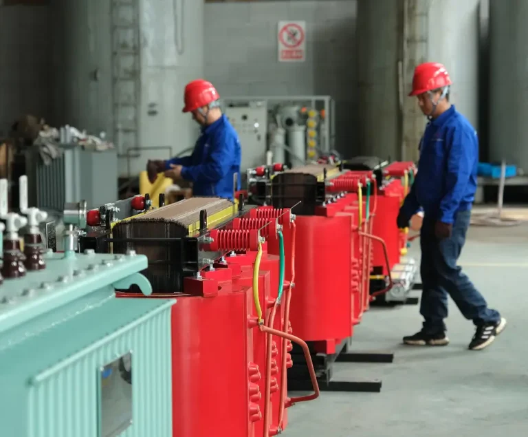 Two BTCN factory workers beside red cast resin dry type transformer assemblies in the workshop